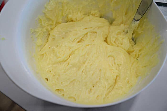 A white bowl filled with creamy yellow carnivore diet cake batter and a metal spoon partially dipped in.