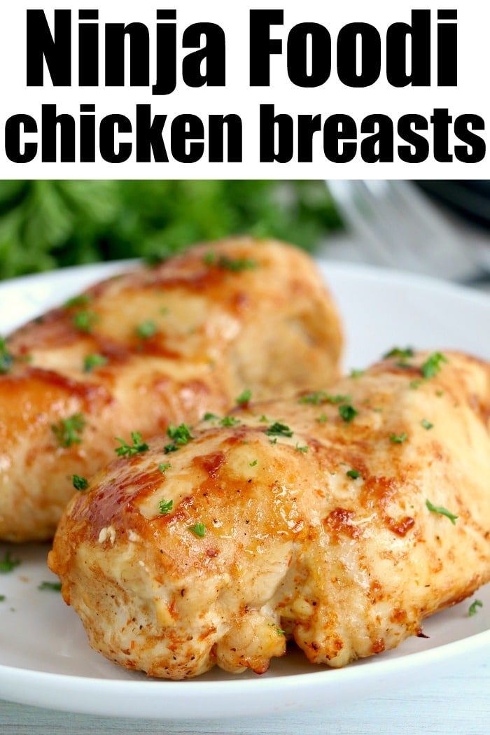 Close-up of two perfectly cooked chicken breasts on a white plate, garnished with chopped herbs. The text at the top reads, "Ninja Foodi Magic: Tender Chicken Breasts.