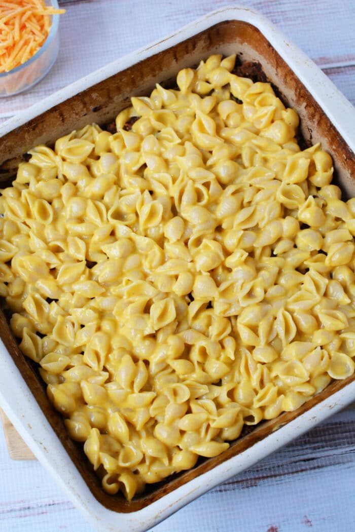 A baking dish filled with creamy mac and cheese made with shell pasta, ready to be baked into a good casserole.
