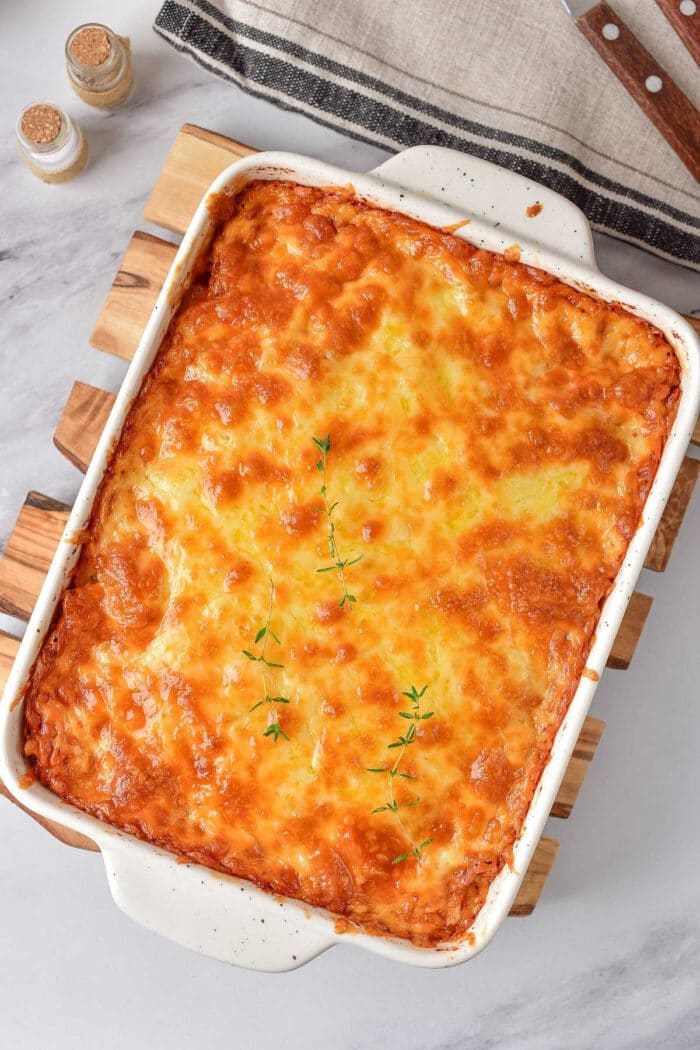 Golden brown baked mac and cheese richness, nestled in a white casserole dish and crowned with fresh thyme sprigs.