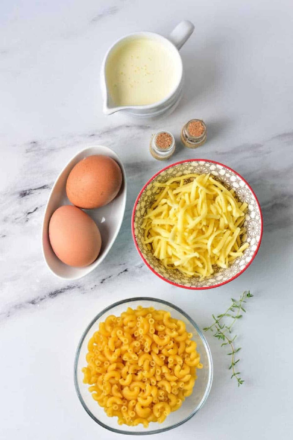 Mac and Cheese with Heavy Cream, shredded cheese, eggs, spices, and thyme arranged on a white surface.