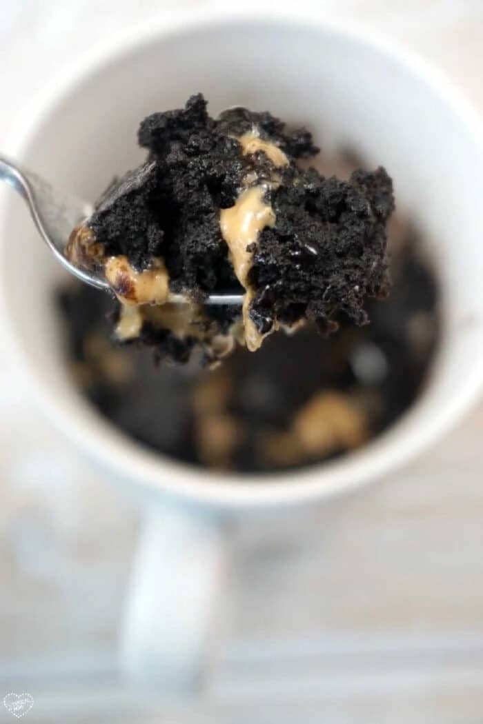 A fork holds a bite of chocolate cake with gooey peanut butter above a white mug, tempting anyone curious about how to make a brownie in a mug.