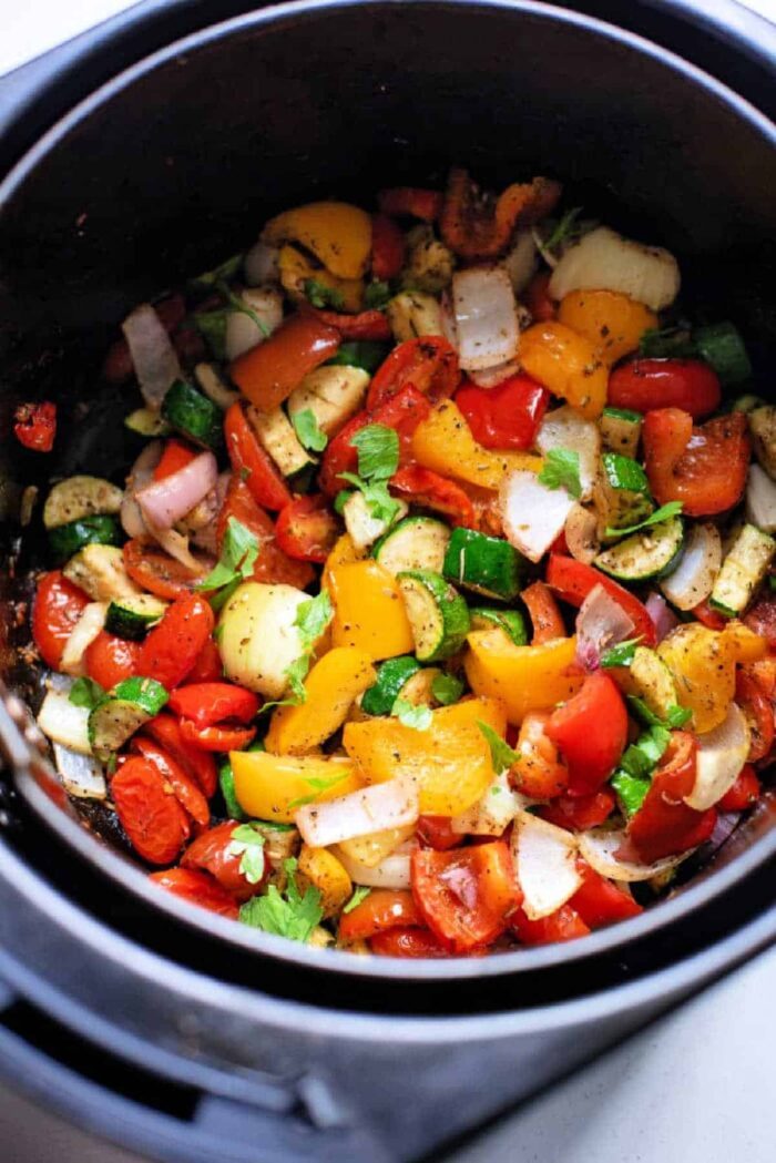 Air fryer brims with vibrant chopped vegetables like peppers, onions, and zucchini, reminiscent of Mediterranean roast favorites.