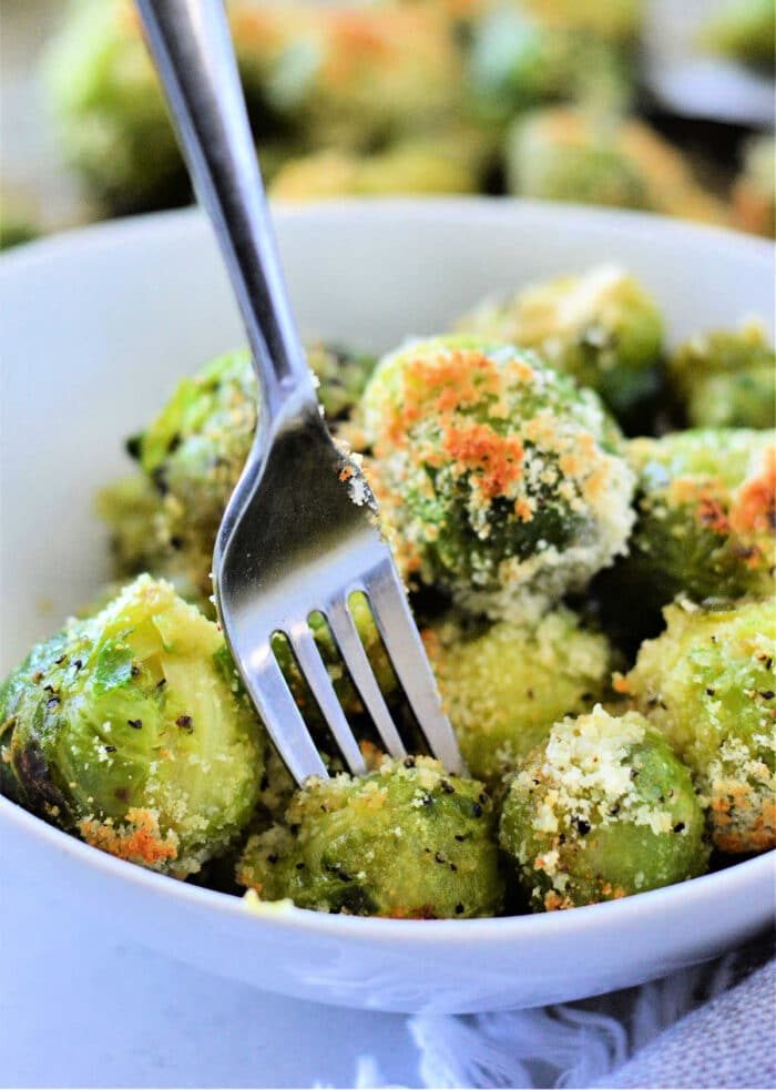 A bowl of microwaved Brussels sprouts with Parmesan cheese, how to microwave Brussels sprouts to perfection, all flawlessly pierced by a fork.
