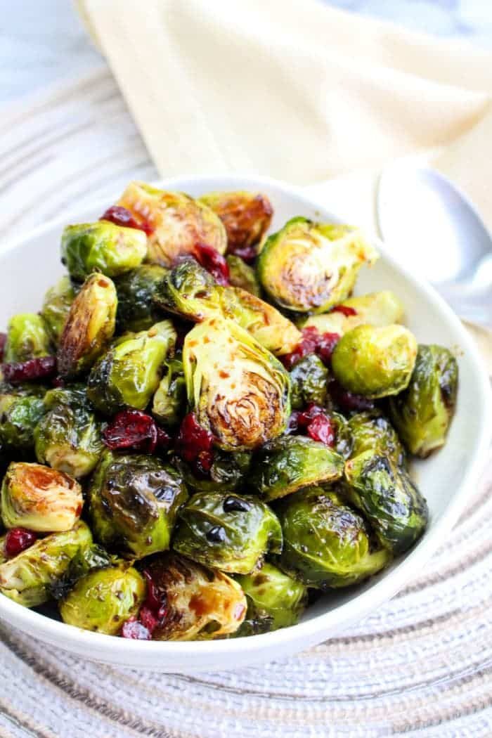 A bowl of Brussels sprouts with cranberries sits on the table, accompanied by a spoon, offering a delightful taste. Discover the ease of preparation by learning how to microwave Brussels sprouts for a quick and good alternative.