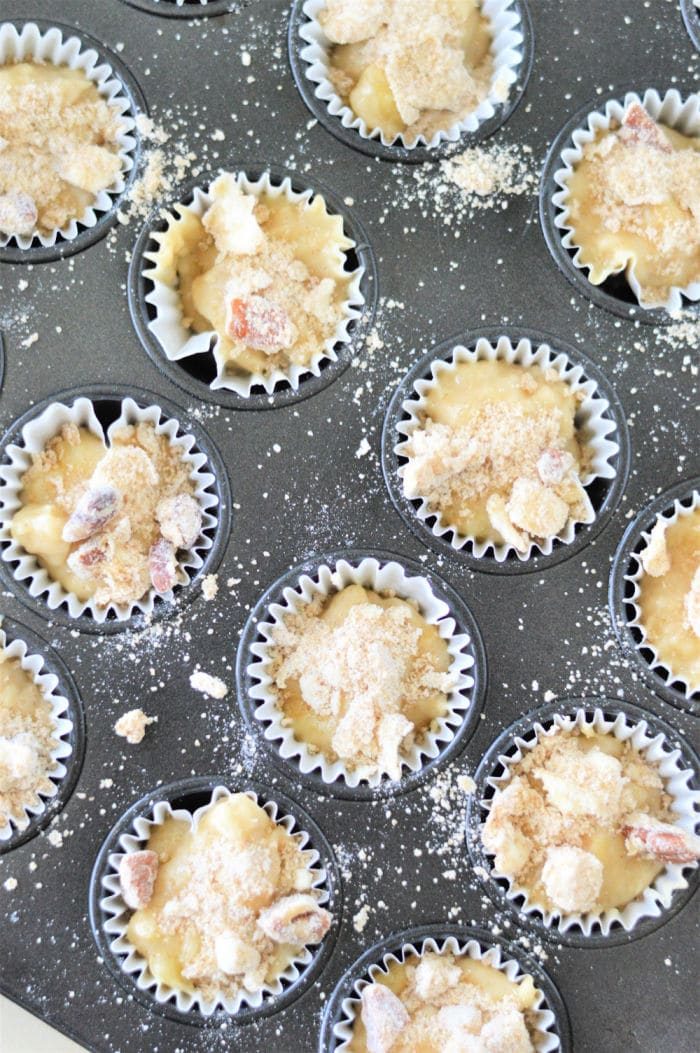 A muffin tray brimming with batter for mini muffins, crowned with streusel toppings, ready to bake.