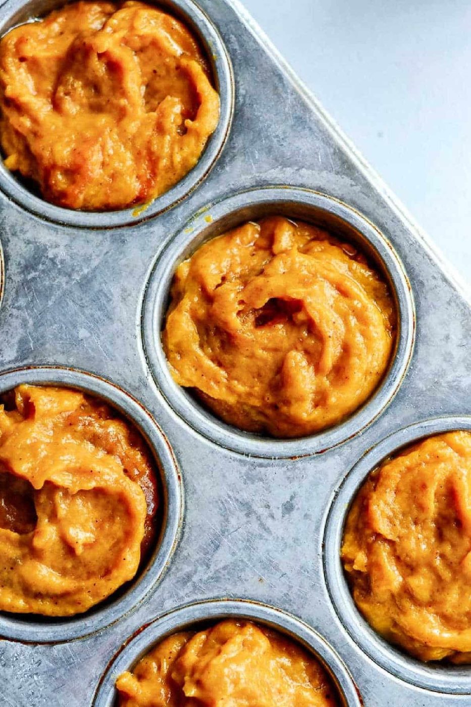 Close-up of a muffin tin filled with unbaked Mini Pumpkin Muffins batter in each cup.