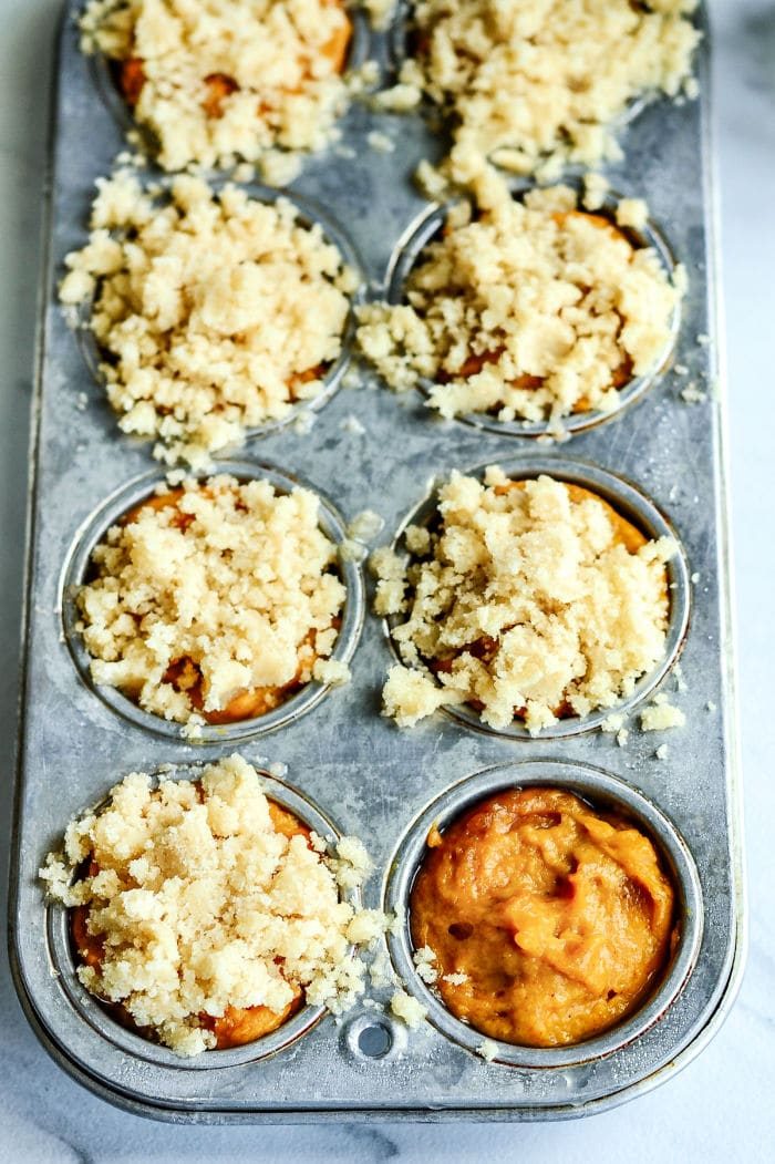 Muffin tin with unbaked mini pumpkin muffins, some topped with crumbly streusel, ready to go in the oven.