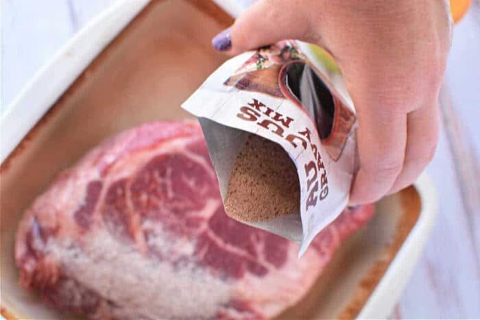 A hand pours dry seasoning mix onto a raw steak in a baking dish, preparing the first step of a flavorful Mississippi Pot Roast Recipe.
