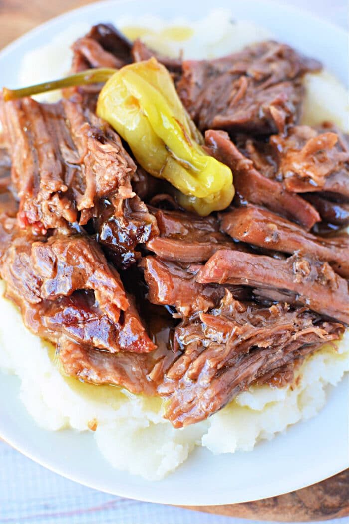 Shredded pot roast on mashed potatoes, topped with a whole pepperoncini and savory brown gravy—our take on the classic Mississippi Pot Roast Recipe.