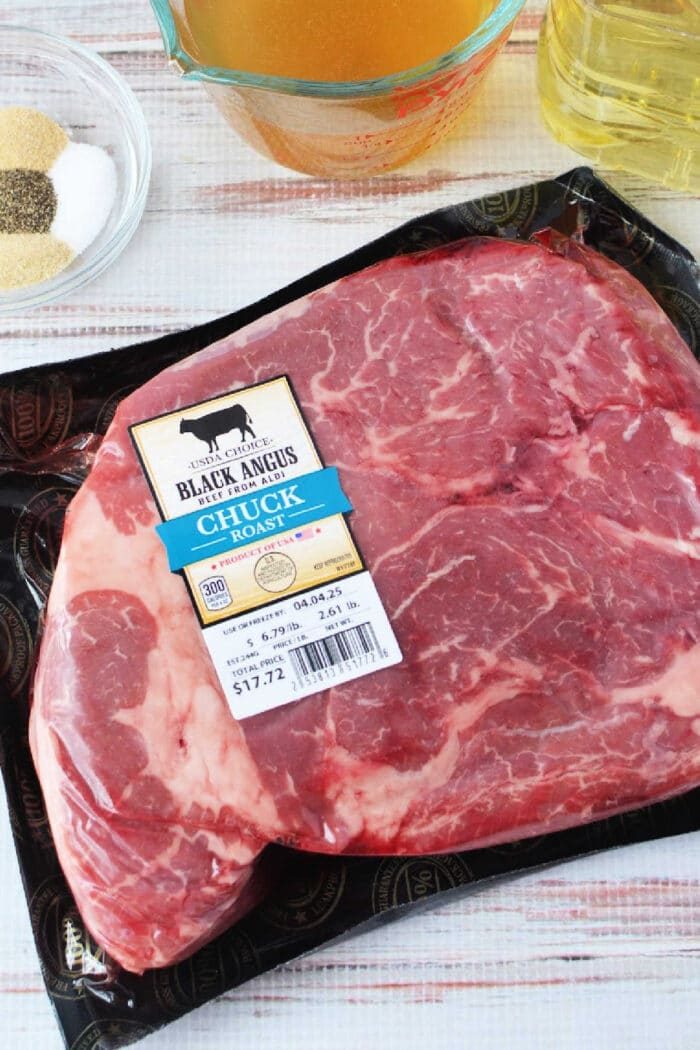 Packaged Black Angus chuck roast on a table with broth, oil, and seasoning bowls nearby—solid for making savory Mississippi roast in your slow cooker.