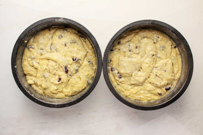 Two round baking pans filled with raw muffin mix batter, speckled with blueberries, to make a cake