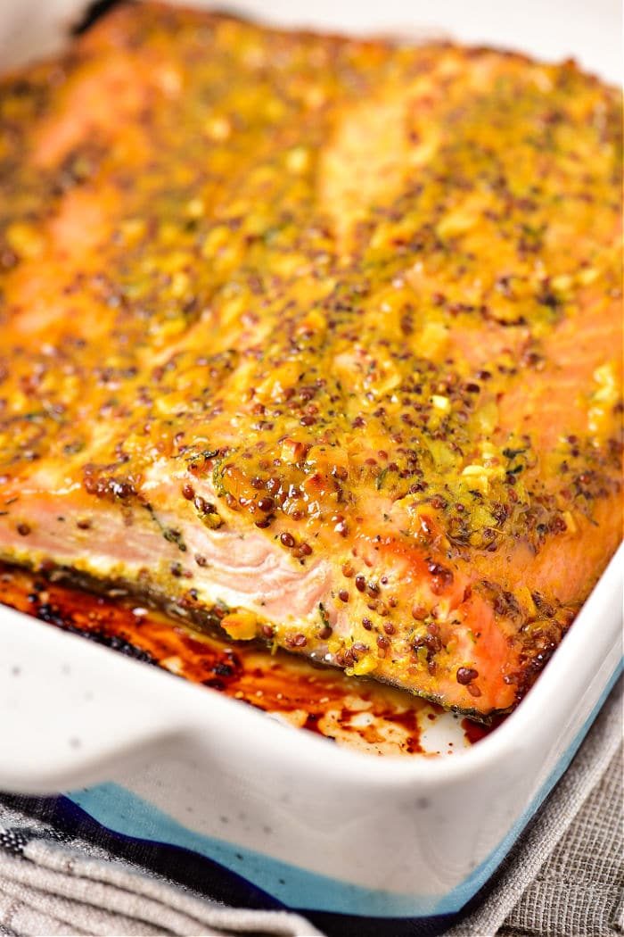 Baked salmon fillet topped with a mustard sauce and herb crust in a rectangular dish.