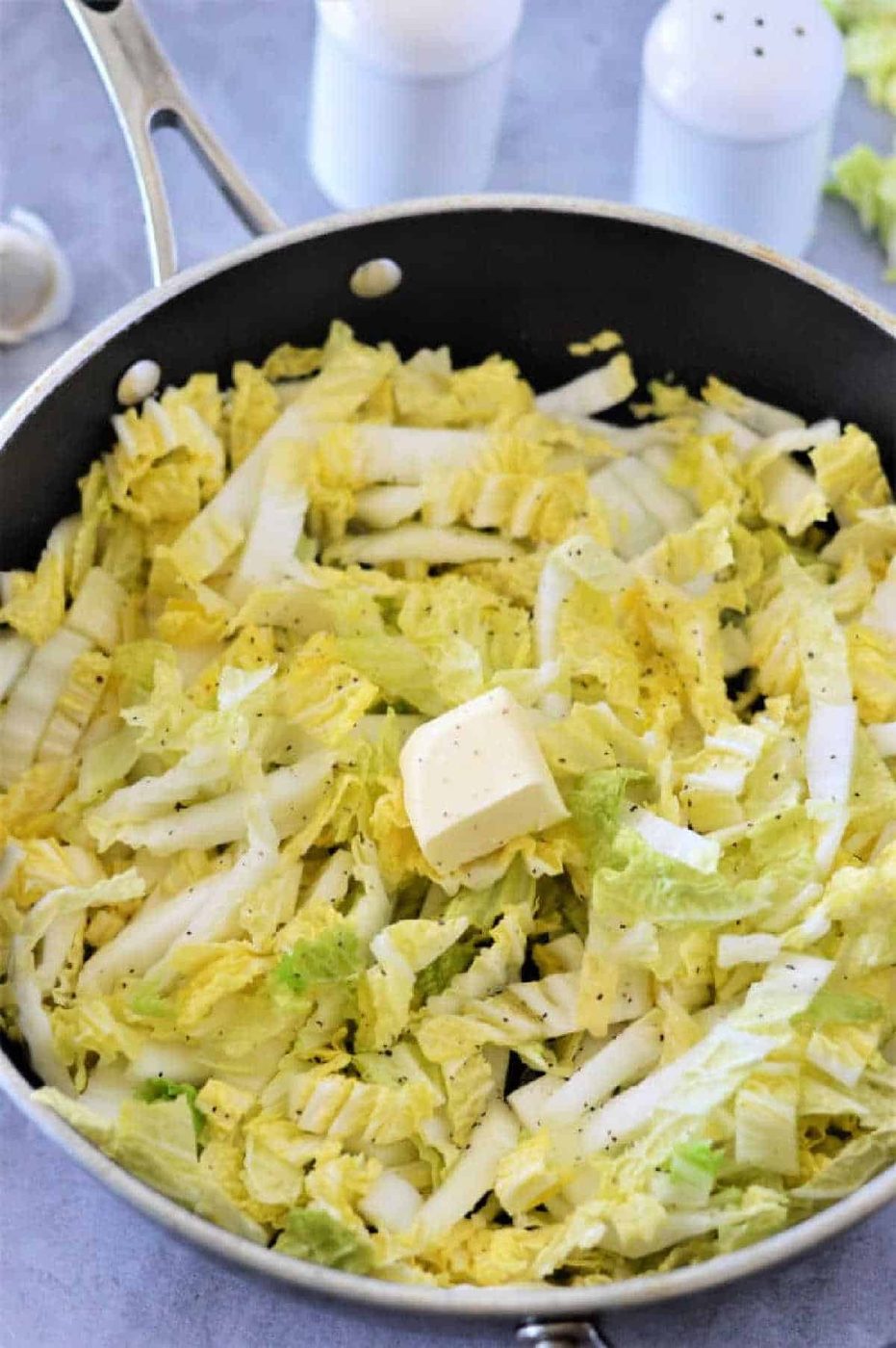Chopped Napa cabbage with a pat of butter and black pepper in a skillet, ready to be cooked—an easy and good Napa cabbage recipe.