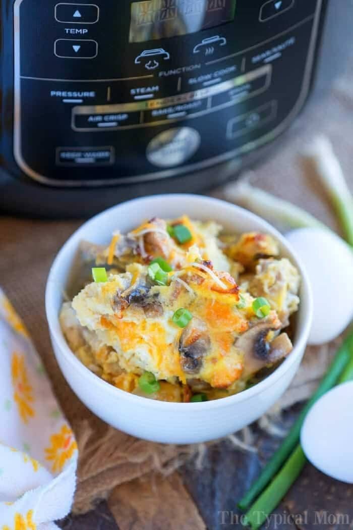 Bowl of cheesy egg casserole topped with green onions in front of a Ninja Foodi, making for a good breakfast, with eggs beside it.