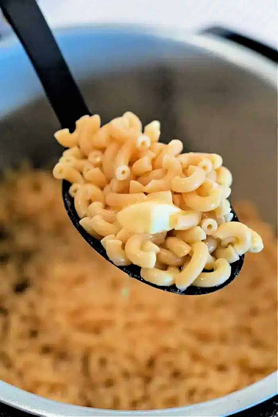 A spoonful of cooked elbow macaroni with a piece of butter, held over a pot of more macaroni—solid for making creamy Ninja Foodi Butter Noodles.