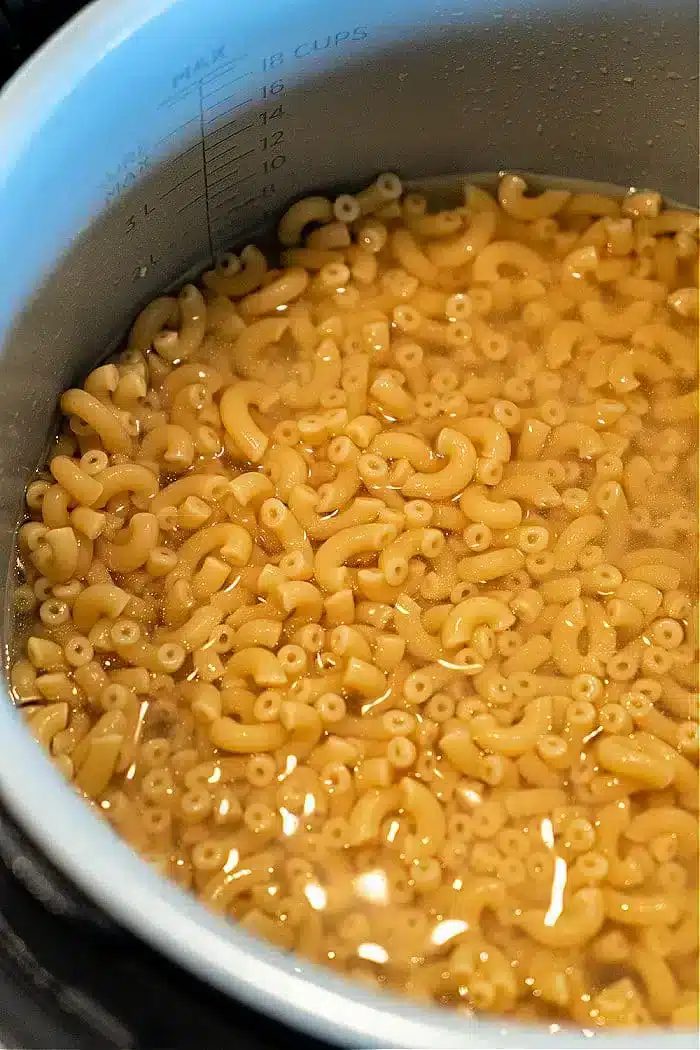 A pot filled with elbow macaroni pasta sits in water up to the 18-cup mark, solid for making a good batch of Ninja Foodi butter noodles, indicating the pasta is being cooked or soaked.