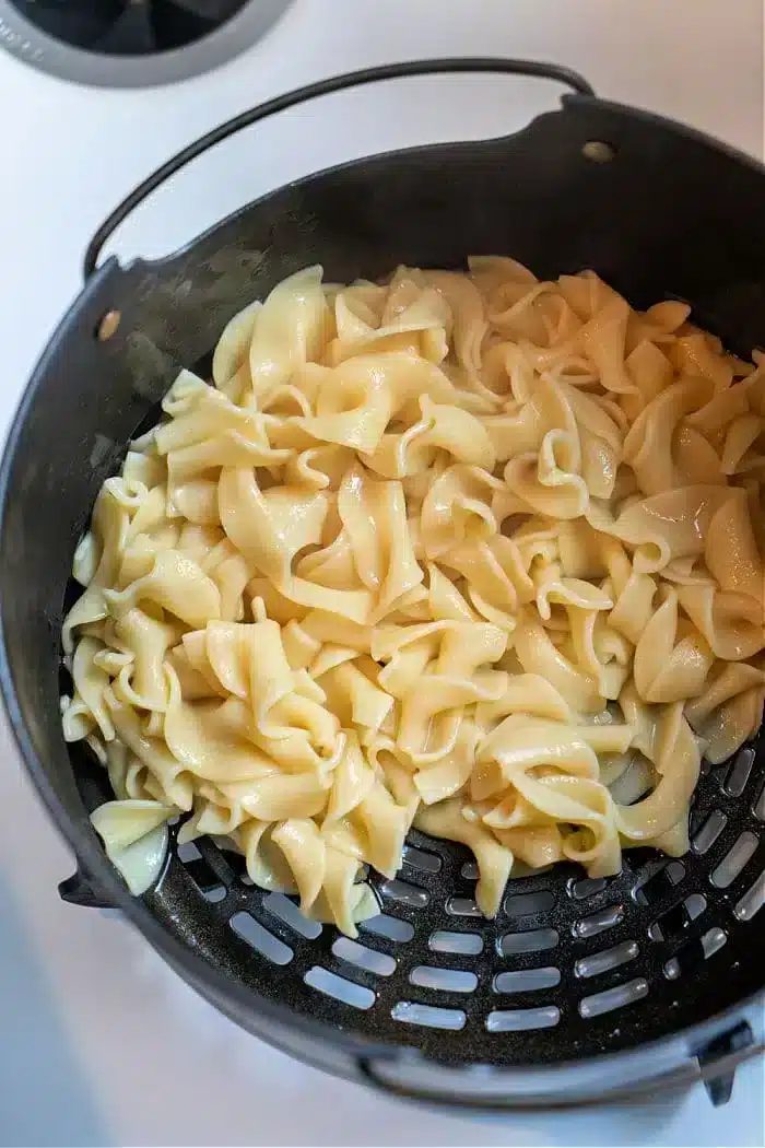 Cooked pasta noodles glisten in a black colander, showcasing their glossy texture from above. Their silky appearance suggests they've been transformed into good Ninja Foodi butter noodles, capturing the essence of creamy perfection as they rest in the strainer.