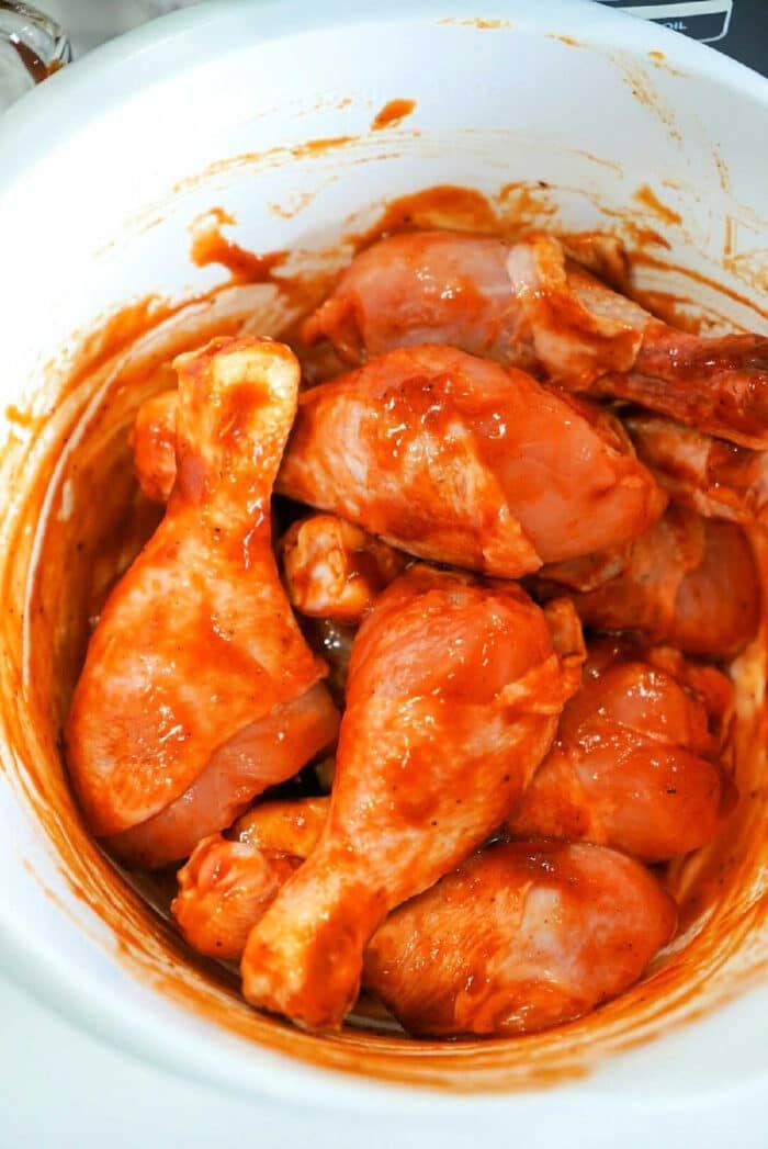 Raw chicken drumsticks coated in a red marinade sit enticingly inside a white bowl, ready to be transformed into a good meal with the Ninja Foodi.