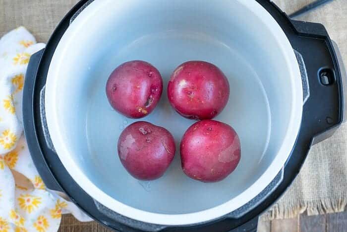 Four red potatoes sit inside an empty electric pressure cooker on a wooden surface, ready to be paired with Ninja Foodi corned beef and cabbage for a hearty meal.