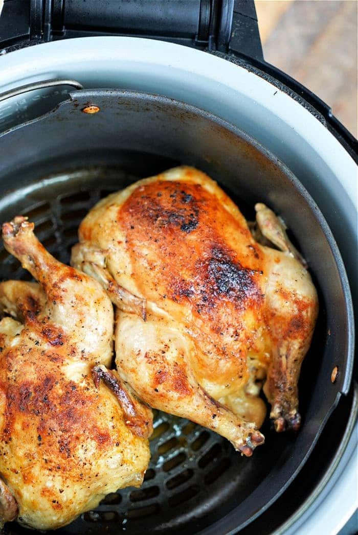 Two golden, crispy-skinned baby chickens nestled in a Ninja Foodi air fryer basket.