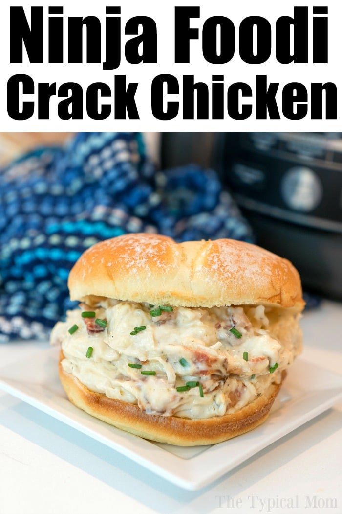 A sandwich filled with creamy chicken and chives lays invitingly on a square white plate. The background showcases a blue checkered cloth and the edge of a kitchen appliance, perfectly capturing the essence of Ninja Foodi Crack Chicken displayed at the top.