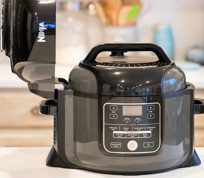 A black Ninja air fryer with its lid open sits on a kitchen counter, solid for trying out your favorite Ninja pressure cooker recipes.
