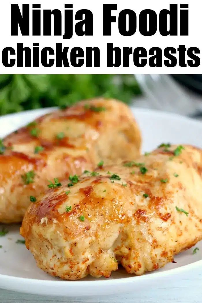 Two cooked chicken breasts on a white plate, garnished with chopped herbs, with text reading Ninja Foodi chicken breasts—a good choice for anyone seeking easy ninja pressure cooker recipes.