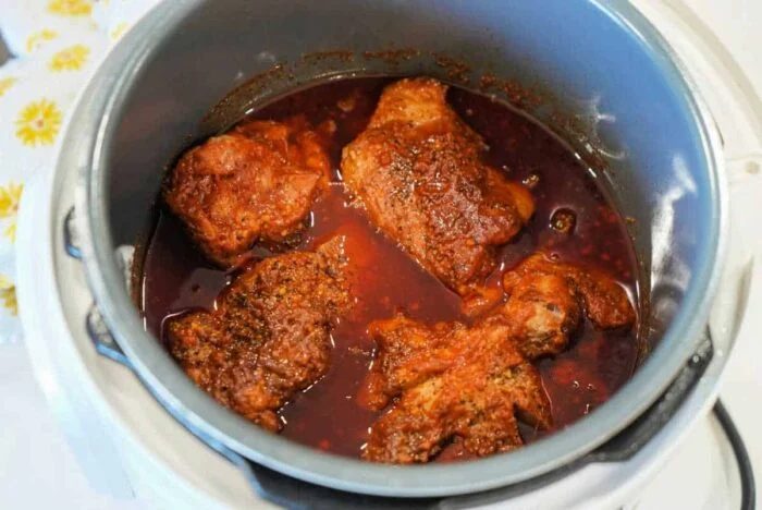 Four pieces of seasoned chicken simmering in red sauce inside a slow cooker, as tender as classic Ninja Foodi pulled pork.