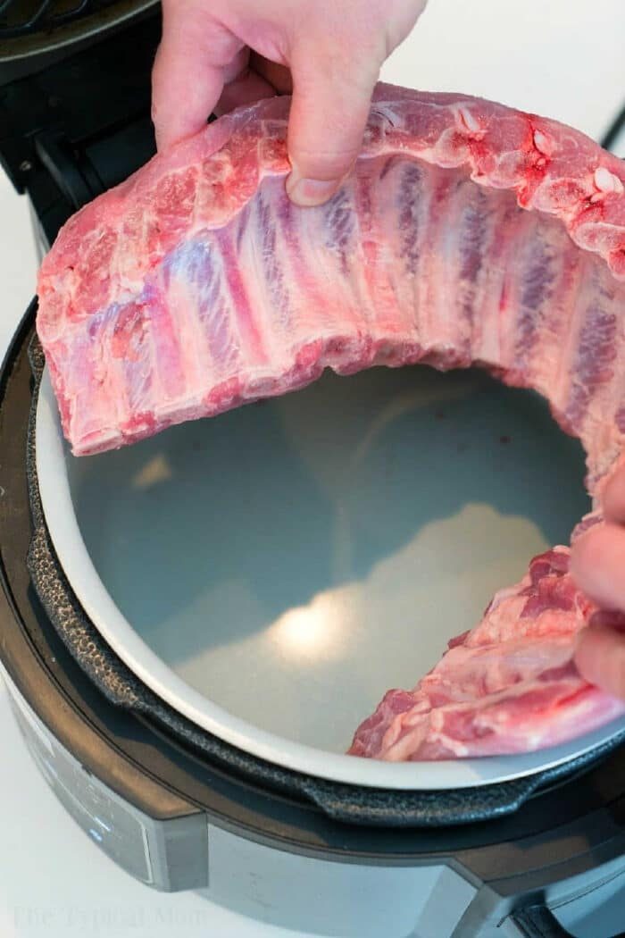 Hands placing a rack of raw ribs into an open pressure cooker, preparing good Ninja Foodi ribs.
