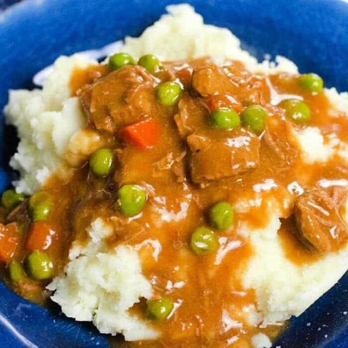 Mashed potatoes topped with hearty beef stew, peas, and carrots, all perfectly cooked in a Ninja Foodi, served on a blue plate.
