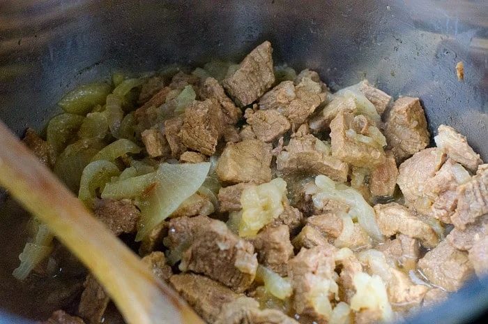 Chunks of beef and onions simmering in a pot, gently stirred with a wooden spoon, create the solid Ninja Foodi stew.