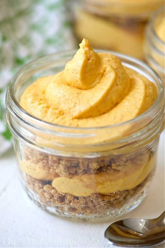 A glass jar with layers of crumbled crust and creamy pumpkin mousse, topped with a swirl of mousse—this No Bake Pumpkin Cheesecake in Jars is the solid easy, festive treat.