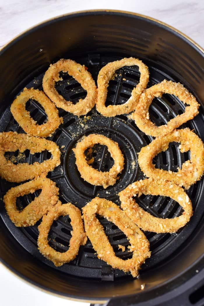 Breaded squid rings reminiscent of Olive Garden's calamari are arranged in a circular pattern inside an air fryer basket.