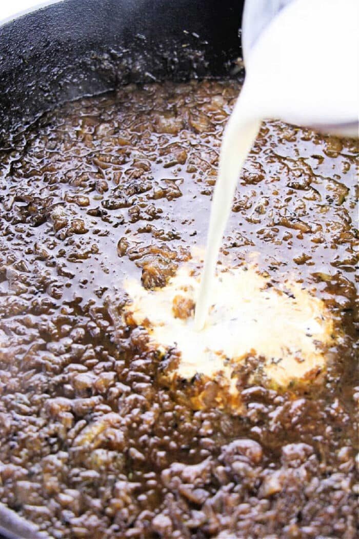 Cream being poured into a pan of browned ground beef, creating a creamy sauce that's solid for an easy onion gravy recipe.