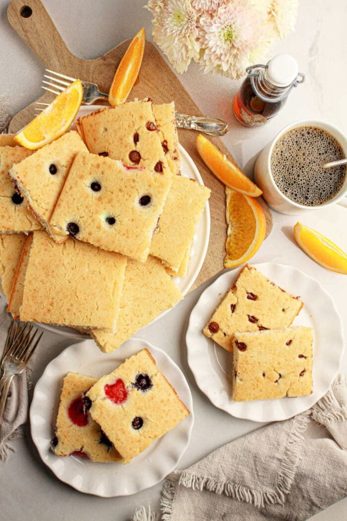 Plates of oven baked pancakes with pancake mix, topped with fruit, orange slices, coffee, and syrup on a table with flowers.