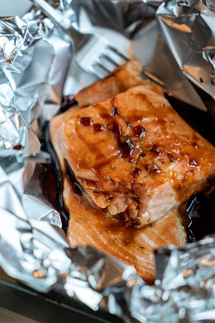 Oven Baked Teriyaki Salmon in Foil, topped with savory sauce, sits beside a fork—perfectly cooked and ready to enjoy.