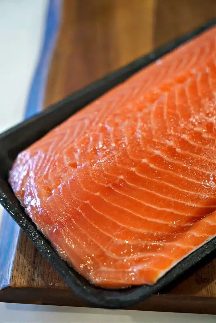 A close-up view of a raw salmon fillet on a dark rectangular tray captures the vibrant orange color and visible marbling, solid for making oven-baked teriyaki salmon in foil. The tray rests elegantly on a wooden surface, ready for its culinary transformation.