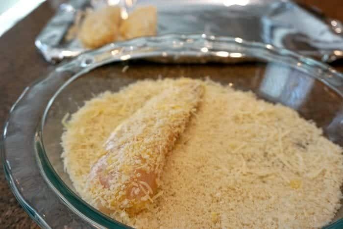 Raw fish being coated in breadcrumbs in a glass dish, with a tray lined with foil in the background—solid preparation for oven fried fish or chicken dinners.