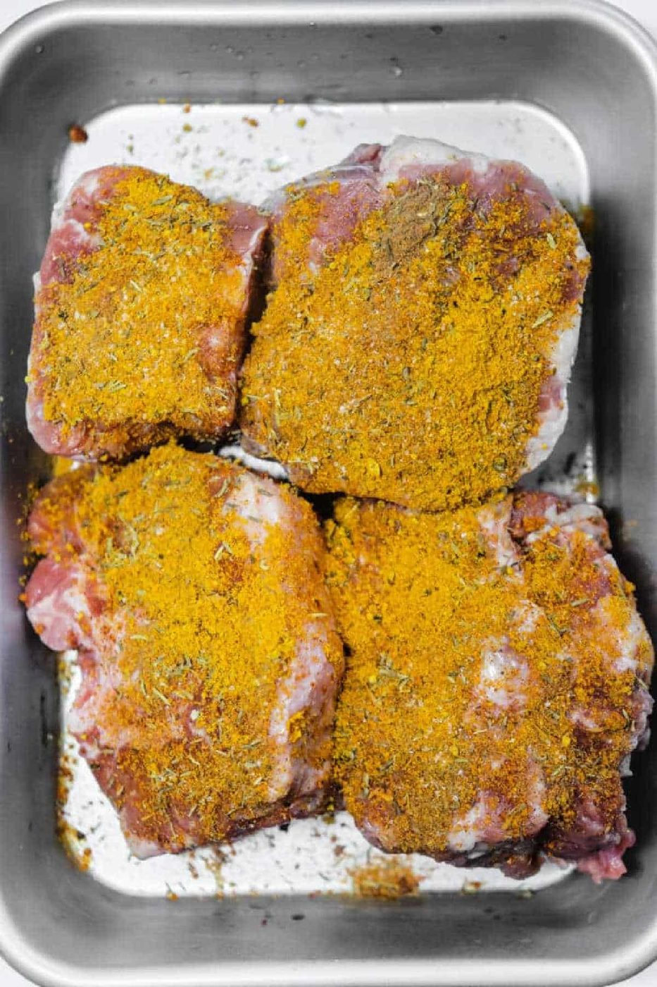 Four raw pieces of meat in a metal tray, coated with a yellow spice rub—solid for preparing a flavorful Oxtail Curry.