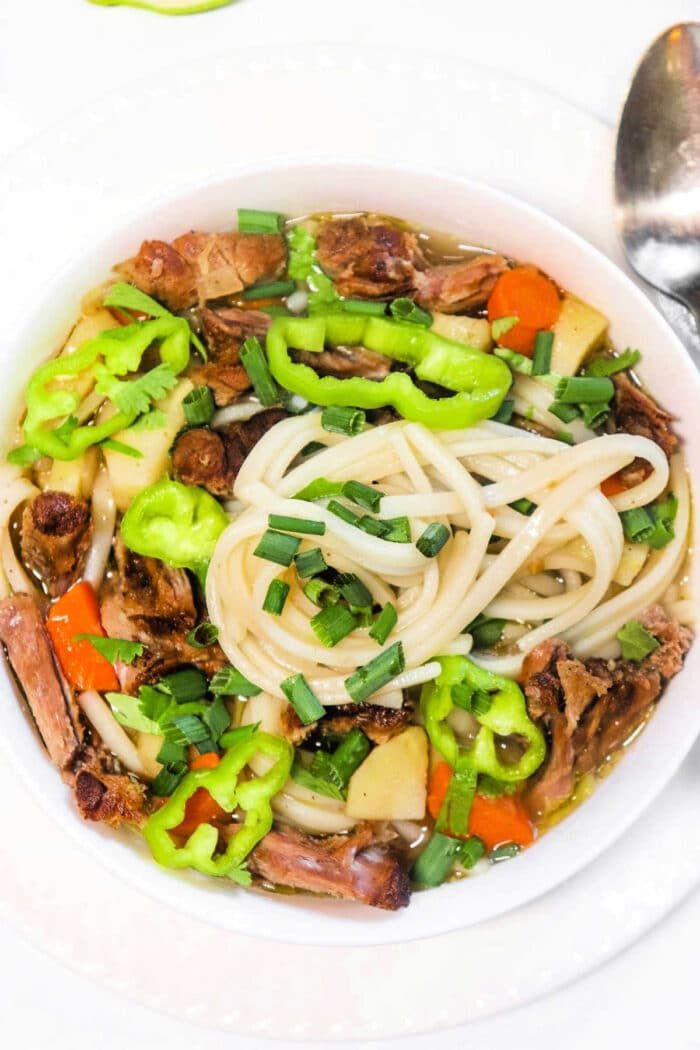 A bowl of oxtail pho brimming with vegetables, beef, and chives, garnished with green peppers.