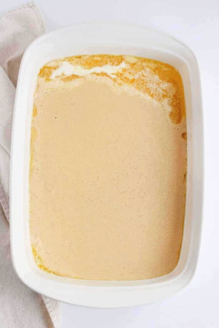 A white baking dish filled with a creamy, light brown liquid mixture, partially set around the edges—solid for making fluffy Pancakes in the Oven.