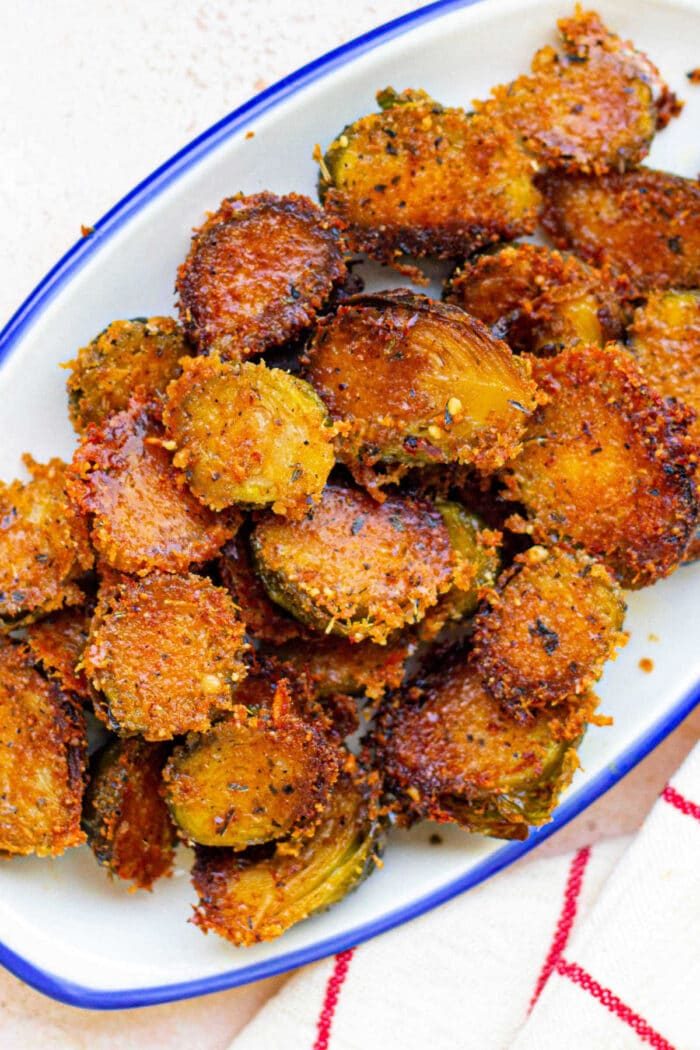 Crispy, golden-brown parmesan brussels served on a white plate with a blue rim, reminiscent of Parmesan crusted Brussels sprouts.