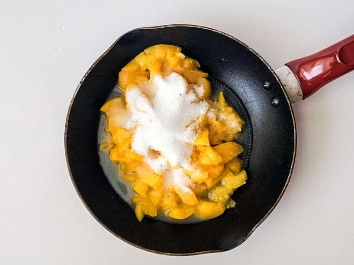 A frying pan with chopped peaches and sugar on a white surface, solid for creating luscious peach bars with a tropical twist.