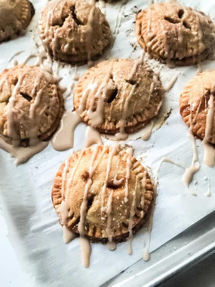 Mini peach hand pies with drizzled icing rest enticingly on a baking sheet.