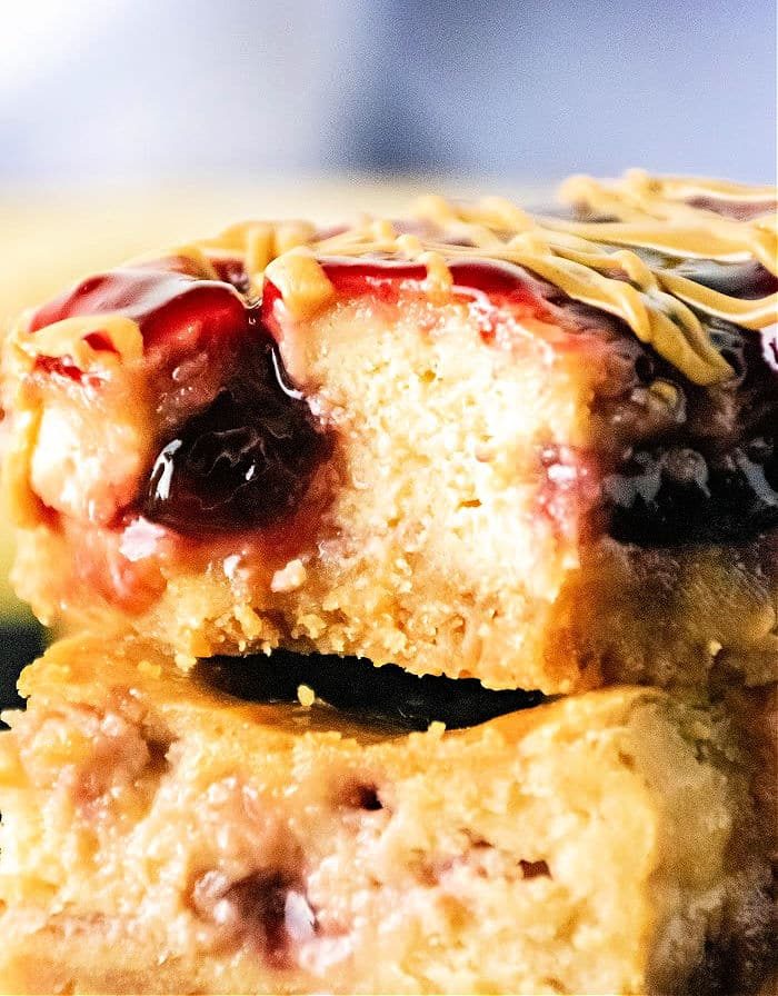 Close-up of Peanut Butter and Jelly Cheesecake Bars, featuring a creamy filling, cherry jam, and a drizzle of peanut butter on top.