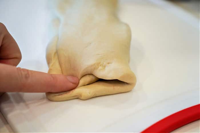 A hand expertly pressing the edge of a folded piece of dough on a white surface, preparing it to create an air fryer beef Wellington masterpiece.