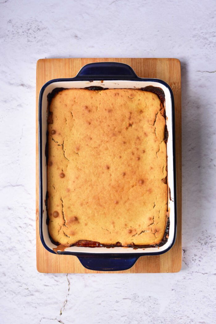 Baked cake in a rectangular blue and white dish on a wooden board, reminiscent of a Pear Upside Down Cake, placed on a textured white surface.