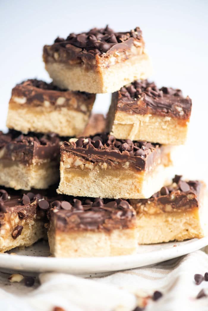 A stack of chocolate and pecan shortbread bars, topped with crunchy nuts, arranged elegantly on a white plate.