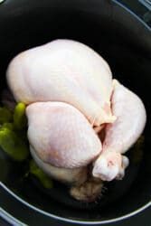 Whole raw pepperoncini chicken with peppers nestled in a black slow cooker.